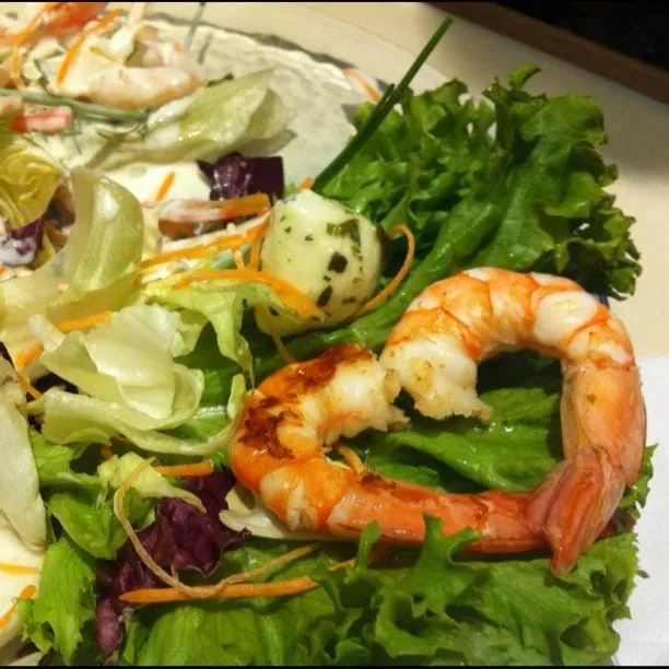 Creveți gătiți aranjați în formă de inimă pe o salată de frunze verzi, cu fâșii de morcov și un scoică marinată.