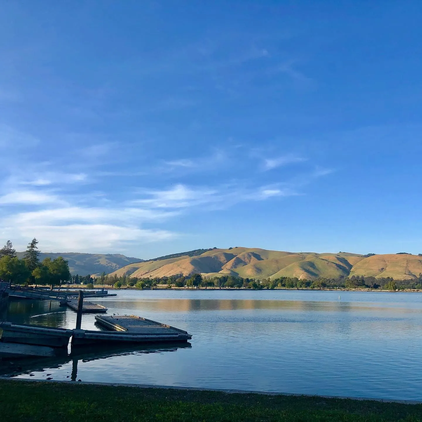 Un lac liniștit, cu pontoane plutitoare și dealuri aurii, se întinde sub cerul albastru și senin din Fremont.