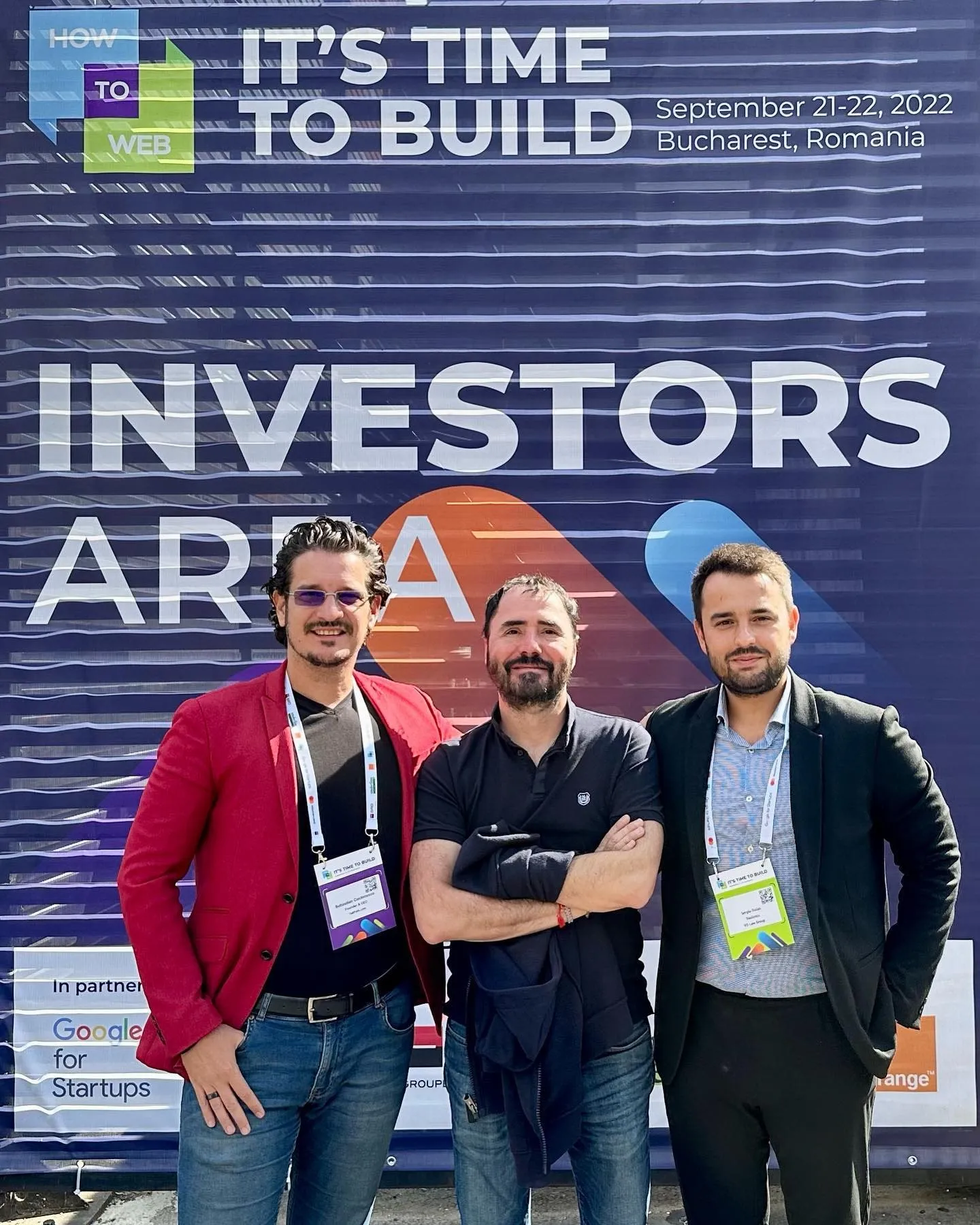 Trei bărbați pozează împreună în fața bannerului How to Web Investors Area din București.