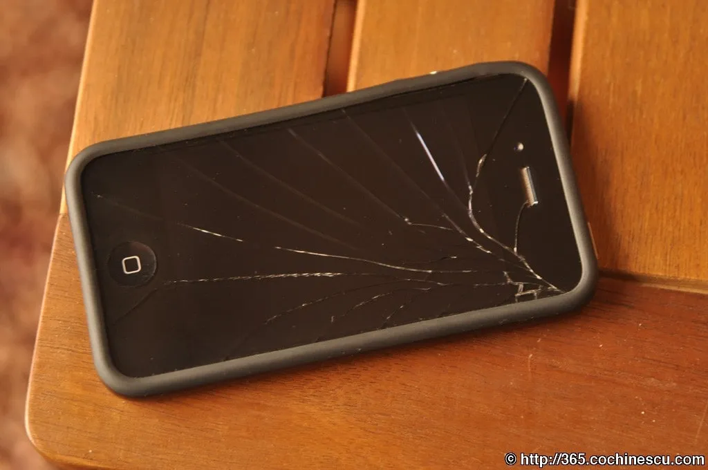 Un iPhone 4 cu ecranul spart este asezat pe o masa din lemn.