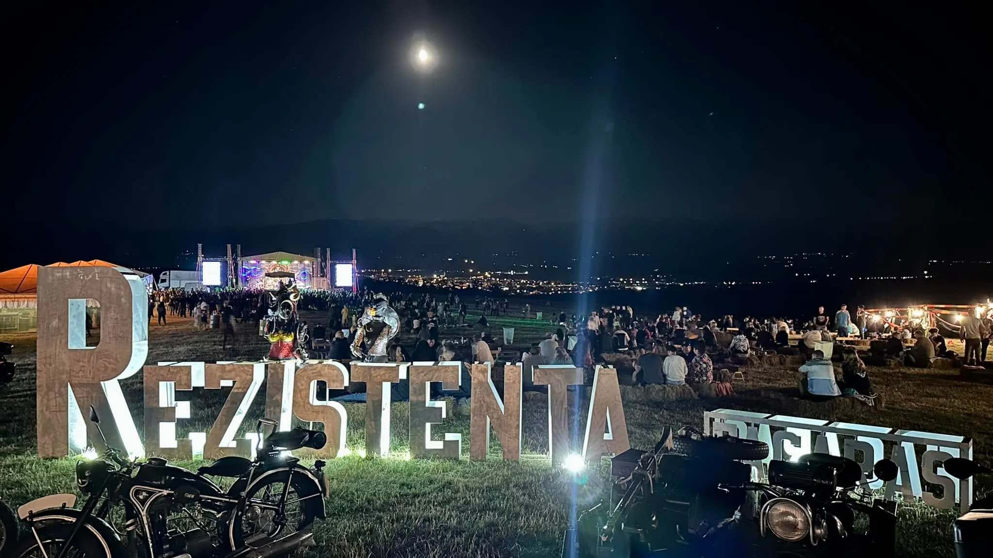 Literele luminoase Rezistenta și Brigadas la un festival în aer liber, noaptea, cu motociclete, mulțime și o scenă sub clar de lună.
