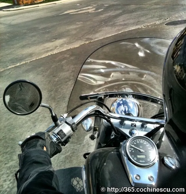 Motociclistul priveste peste ghidonul si parbrizul unei motociclete oprite pe strada.