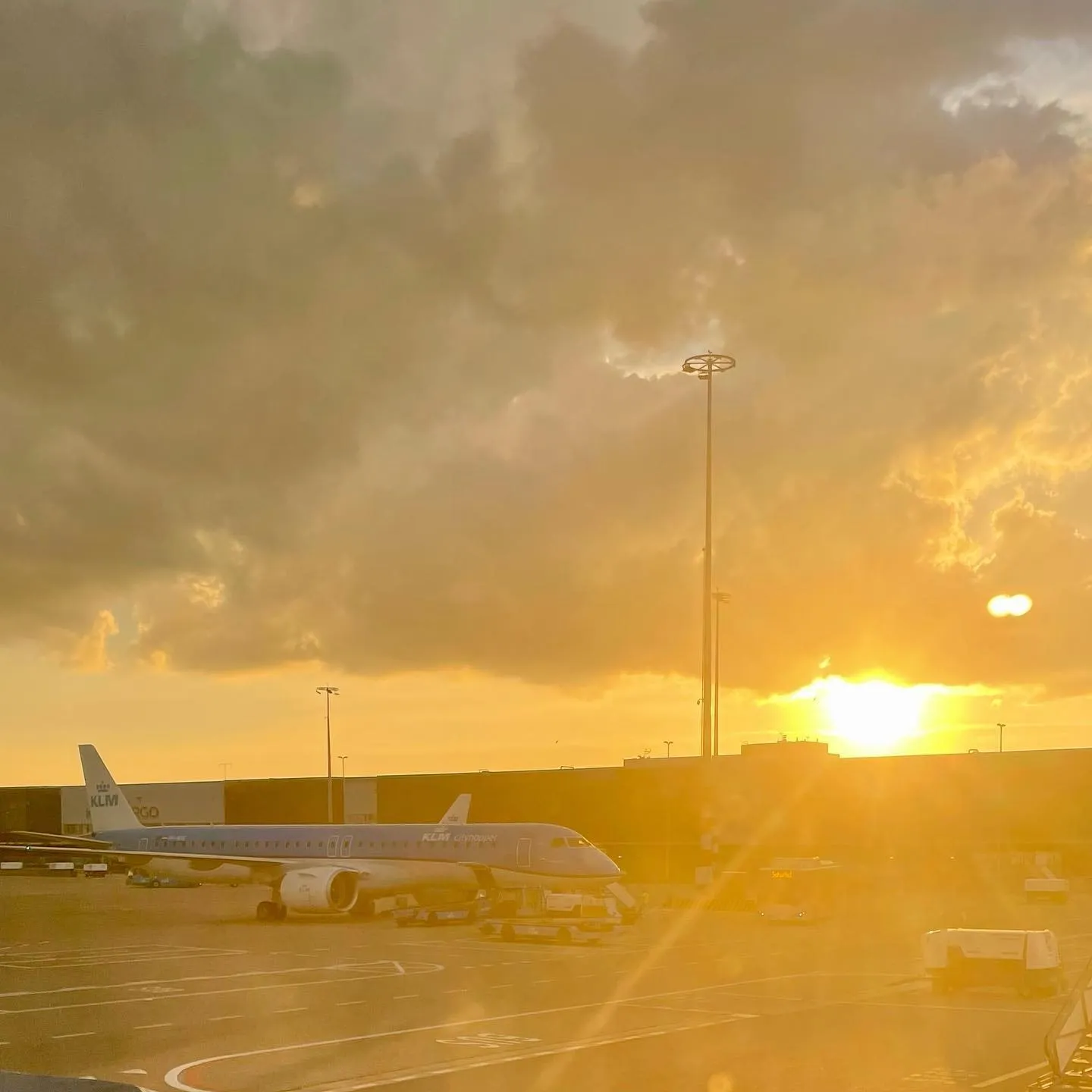 Razele aurii ale soarelui străpung norii grei deasupra unui avion parcat pe un aeroport.