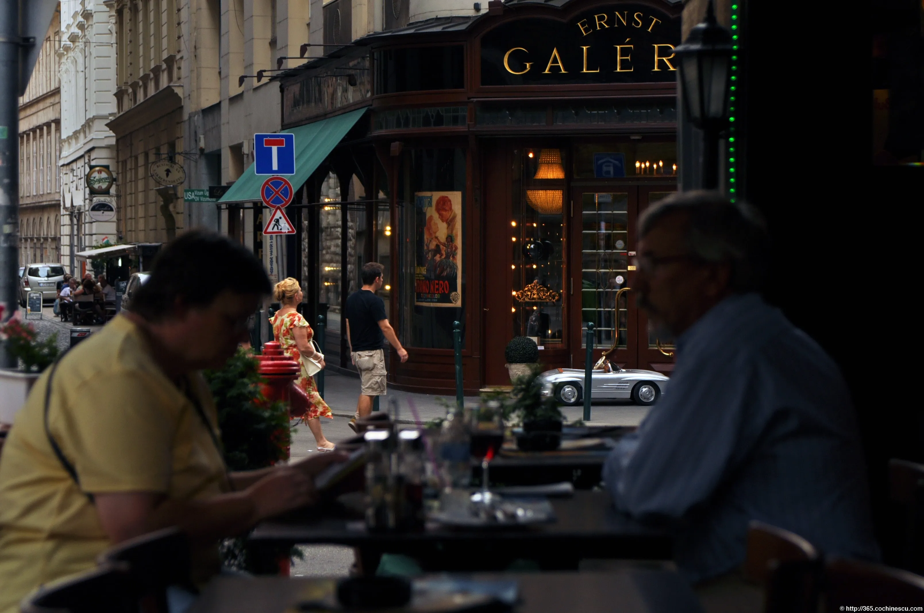 Două persoane stau la masa unei cafenele cu vedere spre o stradă din Budapesta.