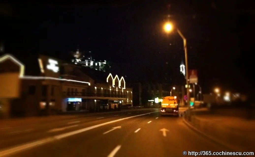 O strada luminata noaptea, vazuta dintr-o masina aflata in mers.
