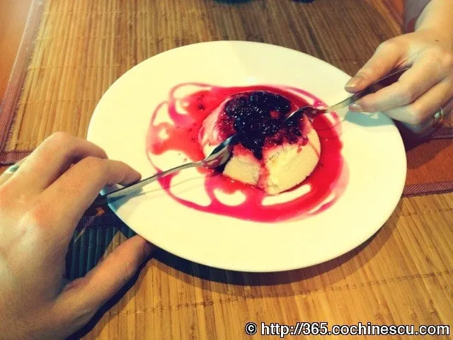 Două persoane împart un desert cu sos roșu și fructe de pădure.