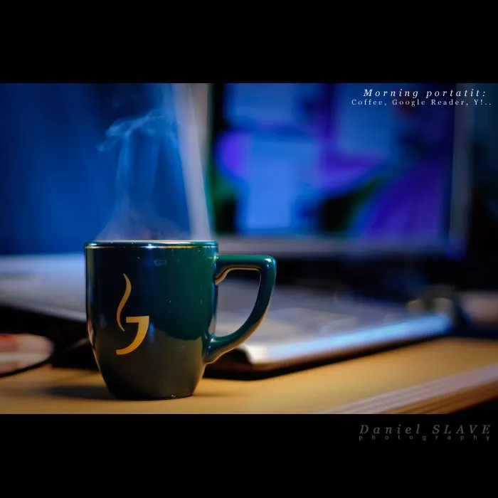 O cana de cafea aburinda se afla pe birou, in fata unui laptop.