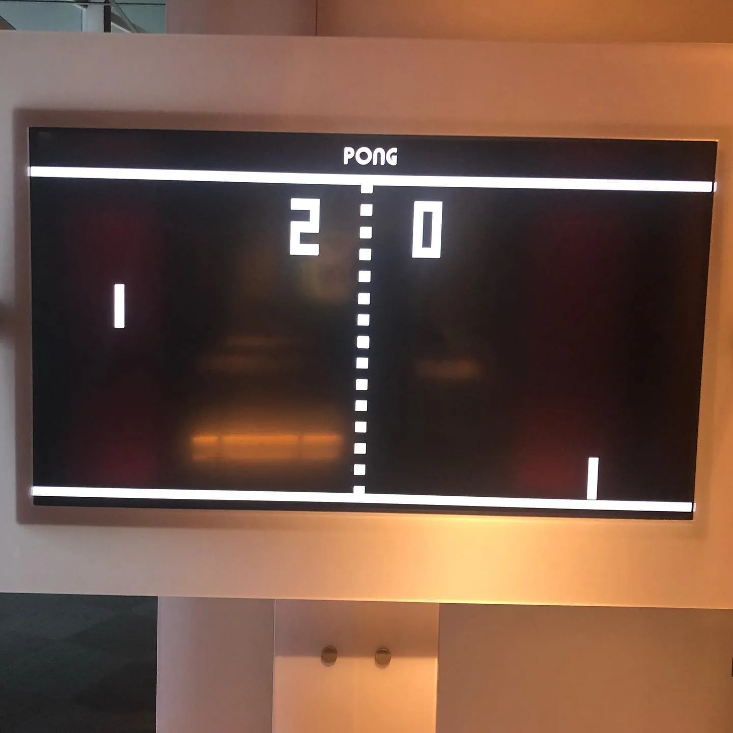 Un ecran montat pe perete afișează clasicul joc Pong, cu scorul de 2 la 0.