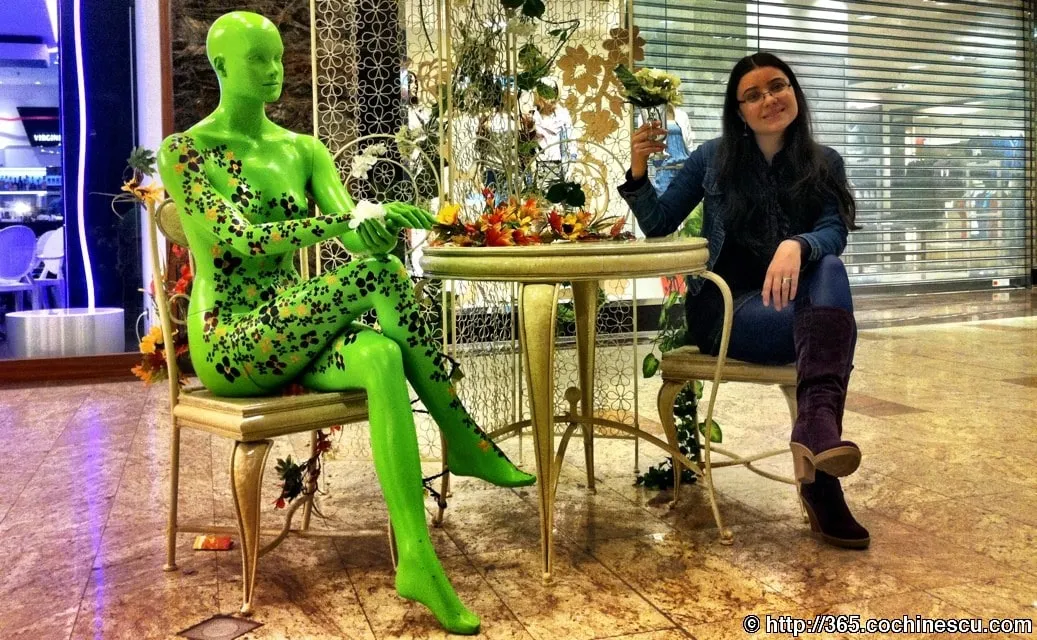 O femeie sta la masa alaturi de un manechin verde decorat cu flori.