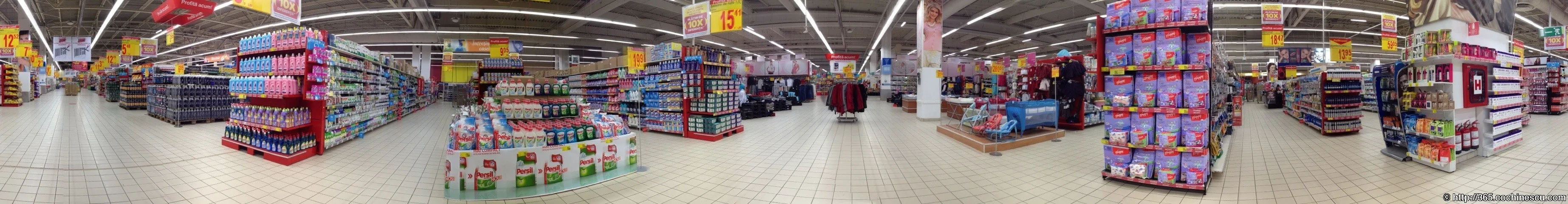 O panoramă largă surprinde raioanele și numeroasele afișe galbene dintr-un supermarket.