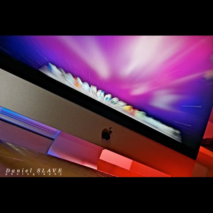 Un computer iMac este fotografiat oblic, in lumini albastre, roz si rosii.