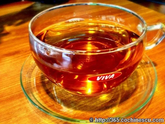 O ceasca transparenta cu ceai de menta este asezata pe o masa din lemn.