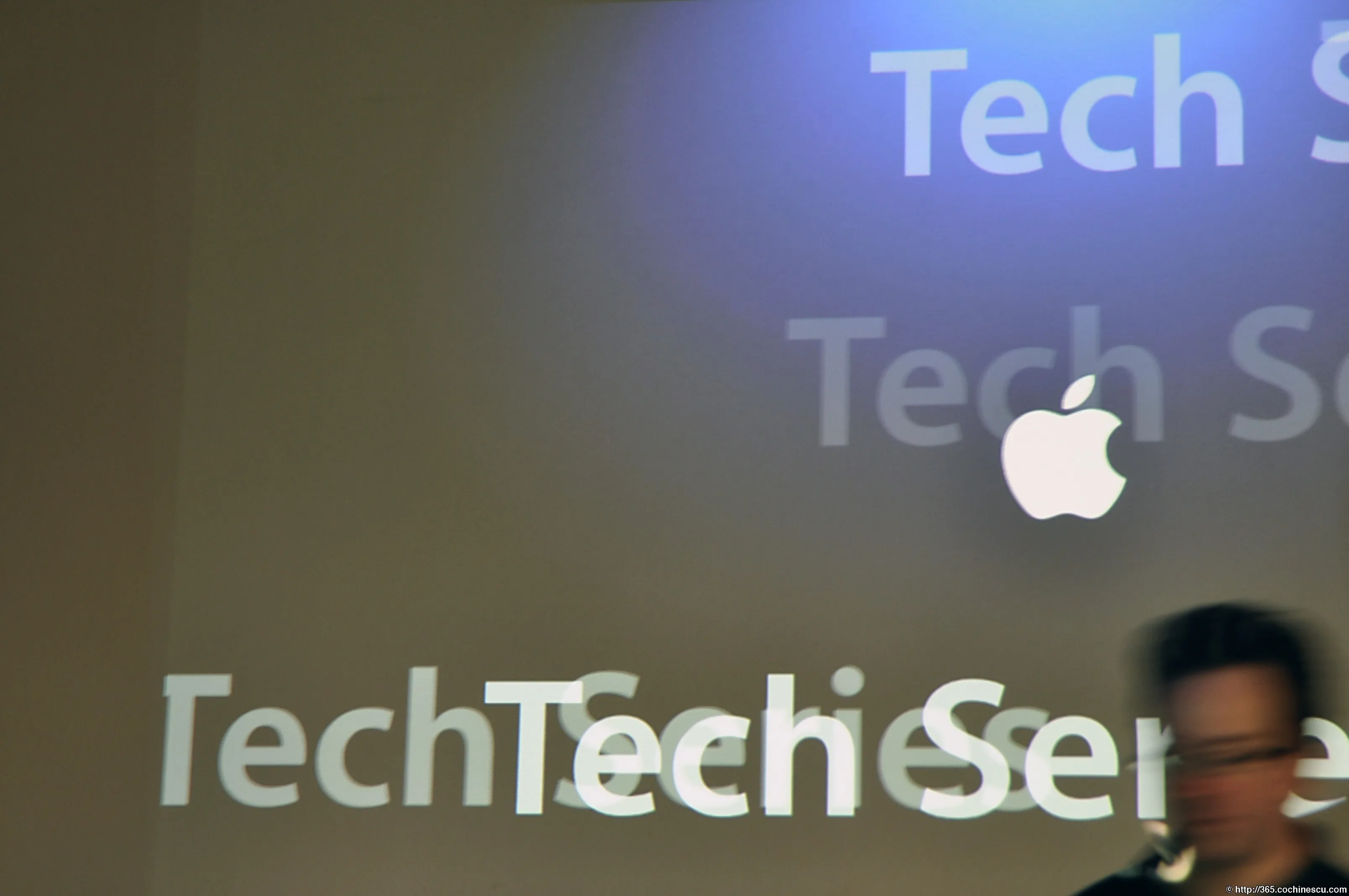 Sigla Apple este proiectată peste textul Tech Series, în timp ce o persoană trece prin cadru.